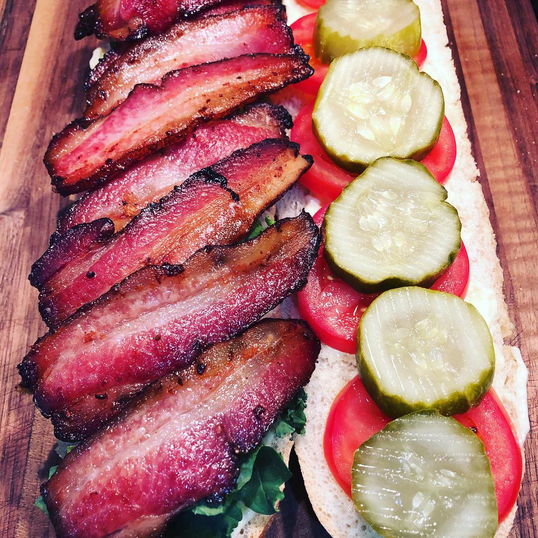 A close up of a bacon sandwich with pickles and tomatoes.